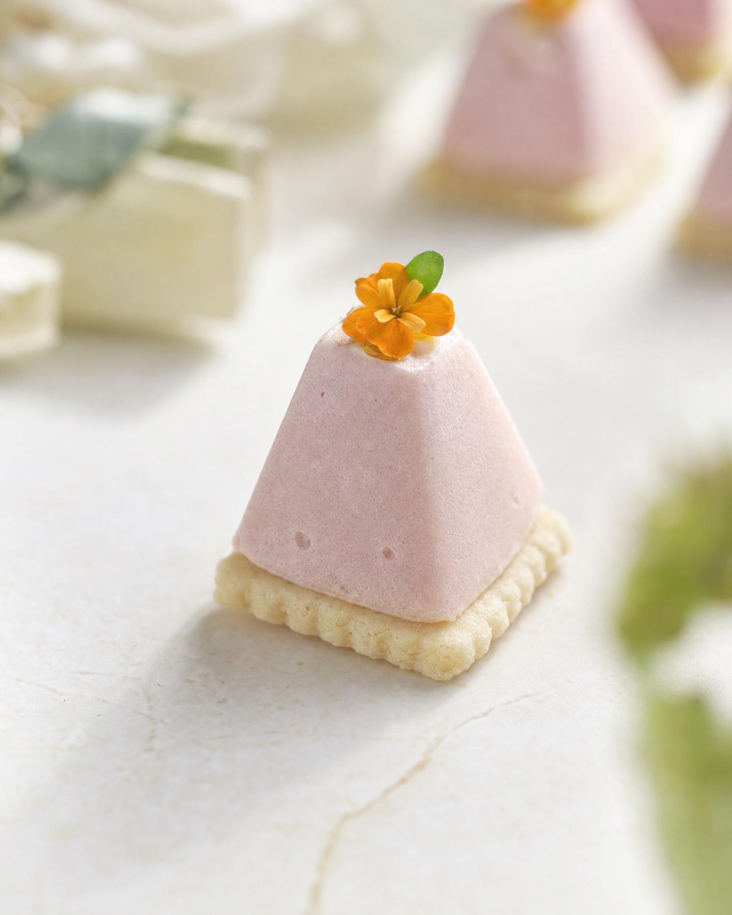 Pyramide de mousse rose pâle sur sablé festonné, coiffée d'une fleur orange et d'une pousse verte