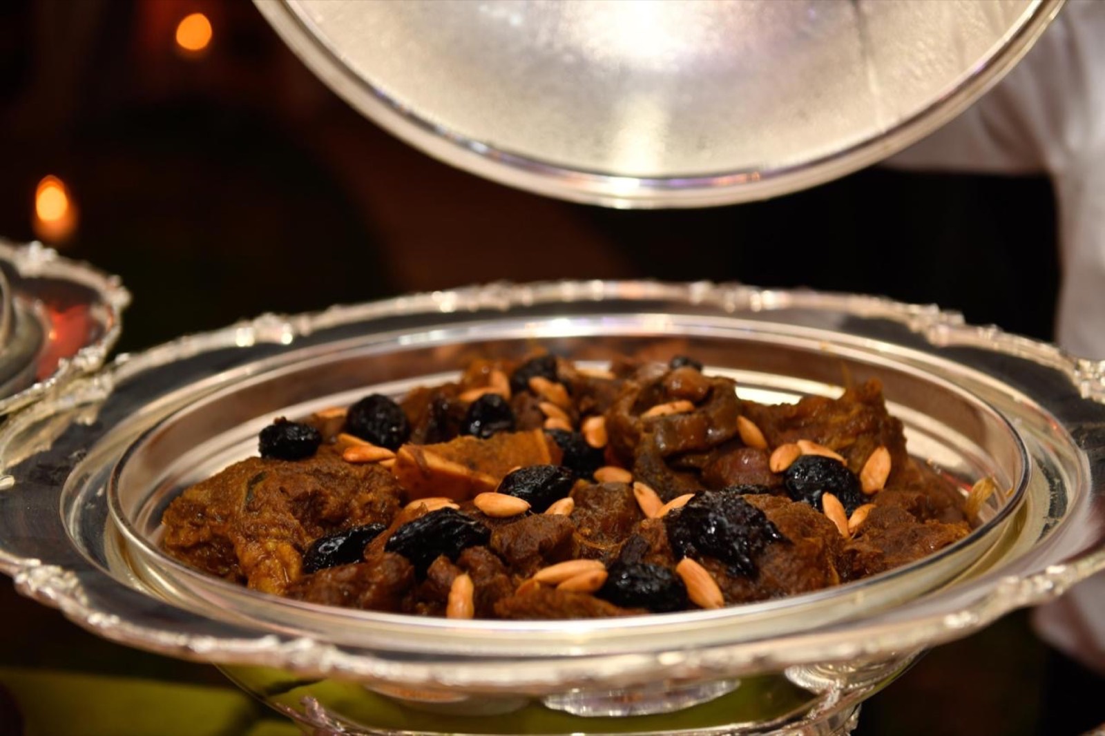Plat d'argent ciselé de viande braisée aux pruneaux et amandes, cloche relevée au-dessus
