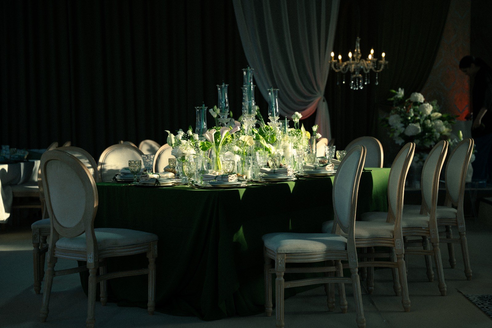 Table de velours vert entourée de chaises médaillon, candélabres de cristal et lustre allumé dans une salle sombre