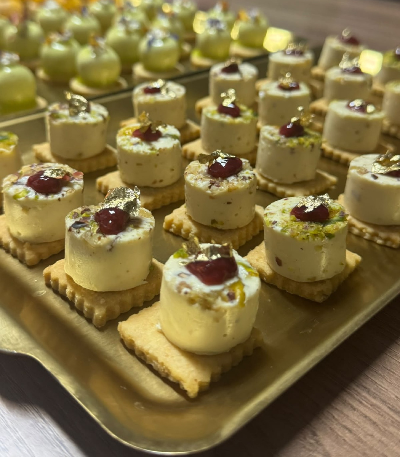 Plateau doré de mignardises au crémeux pistache, chacune surmontée d'une griotte et d'un éclat de feuille d'or