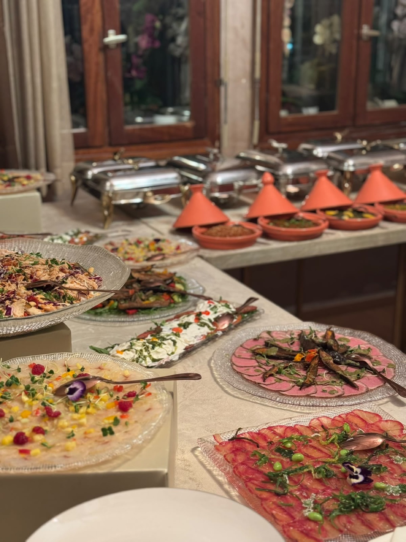 Ligne de buffet froid : carpaccios et salades sur plats de verre, chafing dishes en inox et mini-tagines de terre cuite