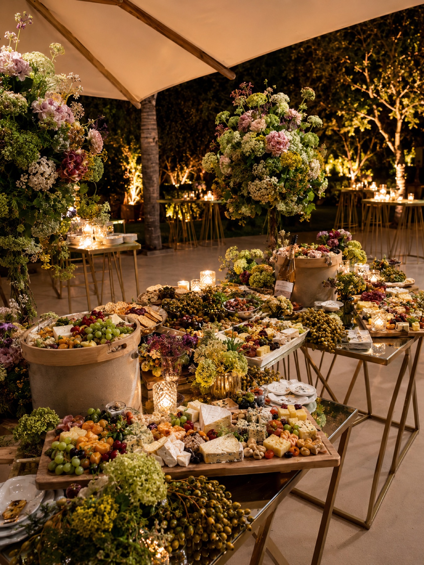 Table de grazing dressée le soir : fromages, raisin et olives sur planches de bois, hauts bouquets et photophores